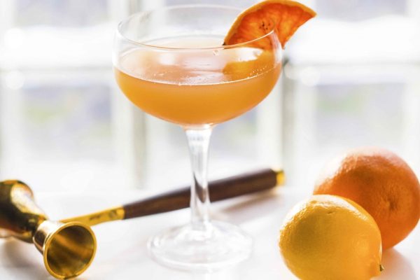 an-orange-cocktail-in-a-glass-sits-on-a-marble-table-with-a-jigger-and-some-fruit-around-it-with-a-a_t20_neBdJA-1-1030x793